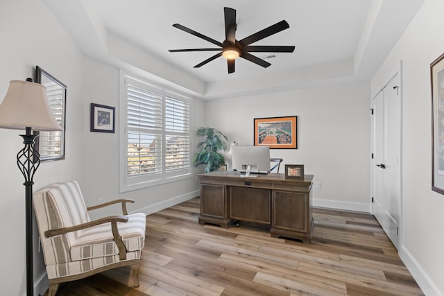 office space featuring ceiling fan, a raised ceiling, and light hardwood / wood-style flooring