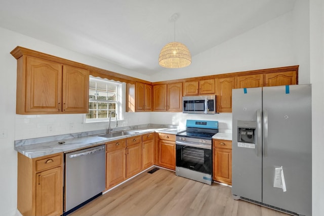 kitchen with light wood finished floors, a sink, lofted ceiling, light countertops, and appliances with stainless steel finishes