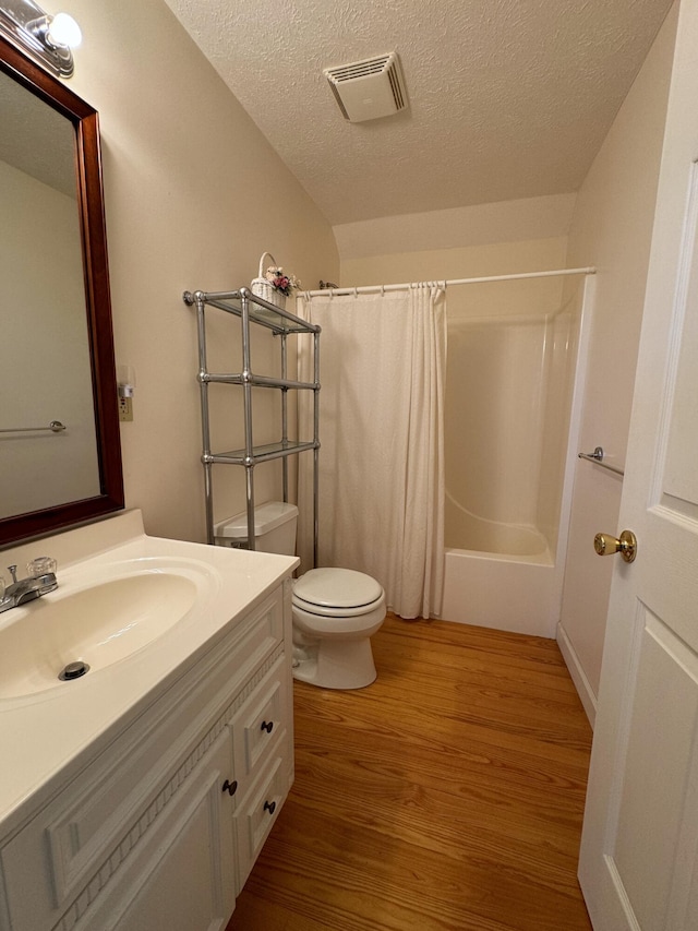 full bathroom with hardwood / wood-style floors, vanity, toilet, shower / bath combo with shower curtain, and a textured ceiling