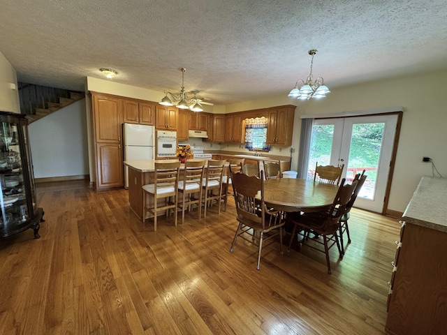 dining space with a textured ceiling, french doors, ceiling fan with notable chandelier, and dark hardwood / wood-style floors