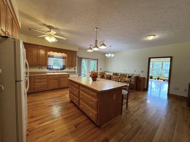 kitchen with a center island, ceiling fan with notable chandelier, white refrigerator, hardwood / wood-style flooring, and decorative light fixtures