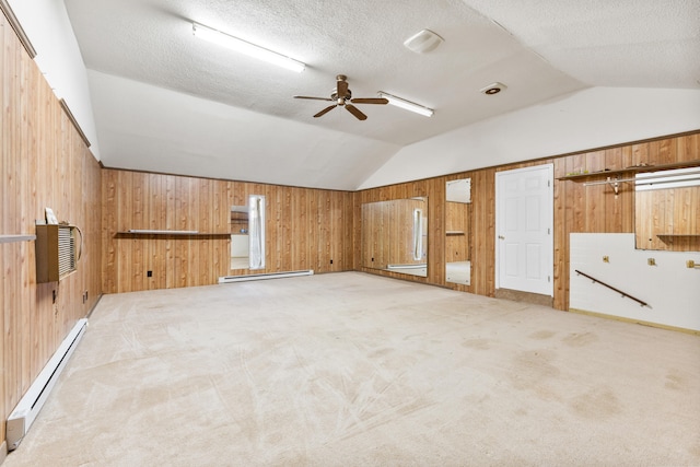 spare room featuring carpet flooring, a baseboard heating unit, wooden walls, and vaulted ceiling