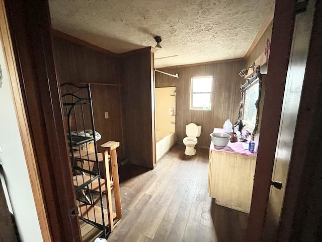 full bathroom with wood walls, a textured ceiling, toilet,  shower combination, and hardwood / wood-style flooring