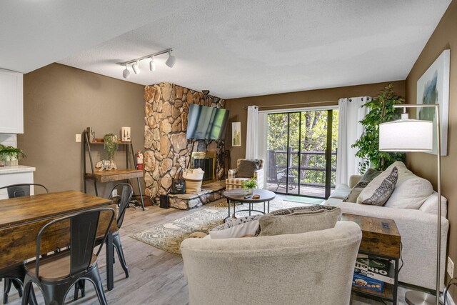 living room featuring light wood-type flooring, a textured ceiling, track lighting, and a stone fireplace