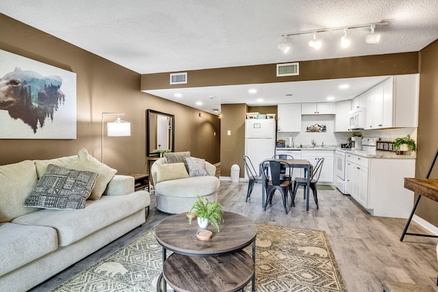 living area with light wood finished floors, track lighting, a textured ceiling, and baseboards