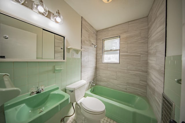 full bathroom with sink, tiled shower / bath, tile walls, and toilet