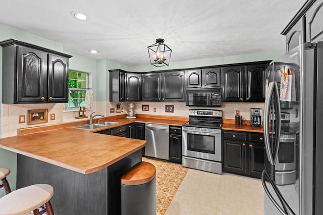 kitchen with a breakfast bar, a sink, stainless steel appliances, a peninsula, and decorative backsplash