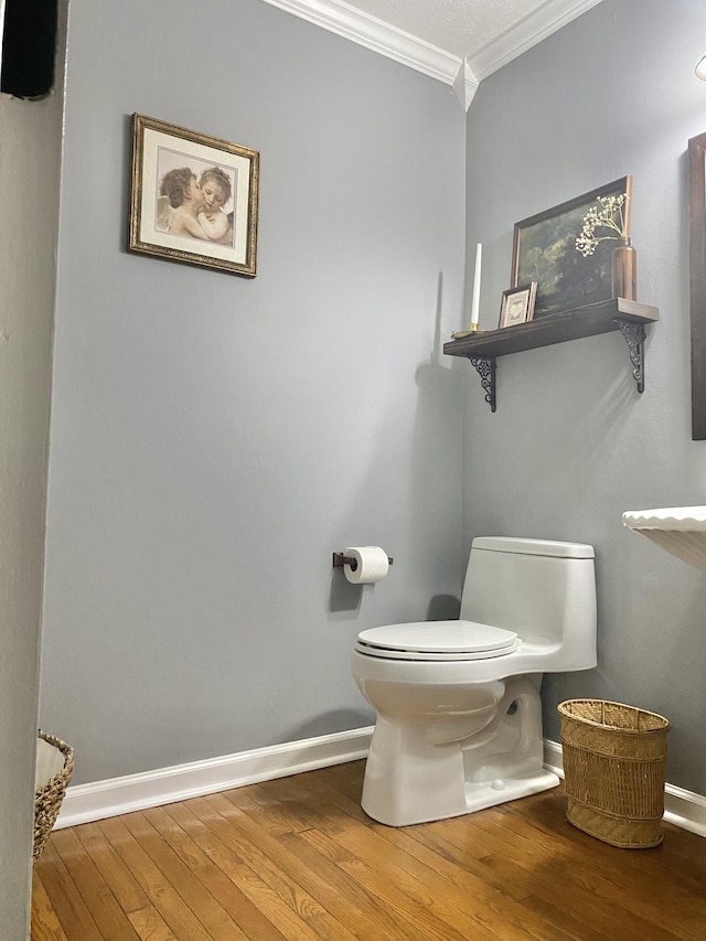 bathroom with crown molding, wood-type flooring, baseboards, and toilet
