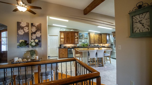 interior space with a kitchen bar, vaulted ceiling with beams, stainless steel fridge, ceiling fan, and beverage cooler