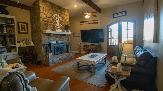 living room featuring beamed ceiling, wood-type flooring, a stone fireplace, and ceiling fan