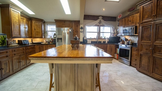 kitchen featuring appliances with stainless steel finishes, tasteful backsplash, butcher block counters, sink, and a center island