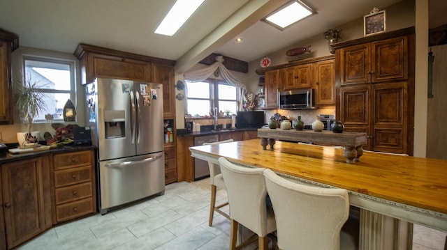 kitchen featuring wooden counters, stainless steel appliances, tasteful backsplash, a kitchen bar, and vaulted ceiling