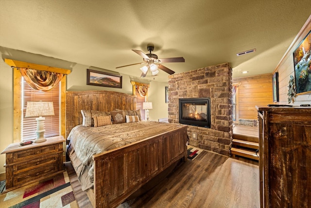 bedroom with a fireplace, a textured ceiling, ceiling fan, and wood walls