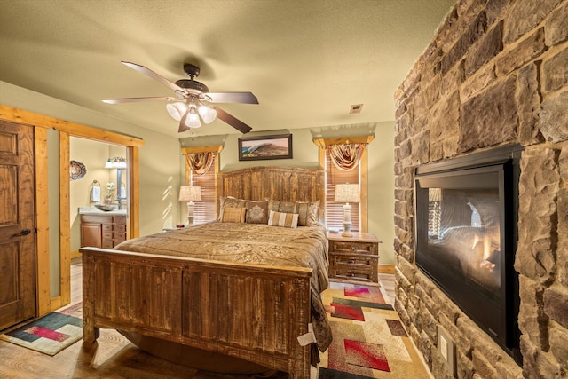 bedroom featuring ceiling fan, light wood-type flooring, a textured ceiling, and ensuite bath
