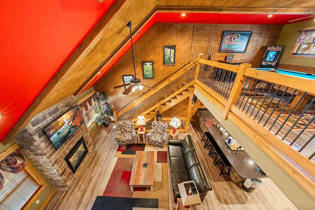 living room featuring a fireplace, a towering ceiling, ceiling fan, and wood walls