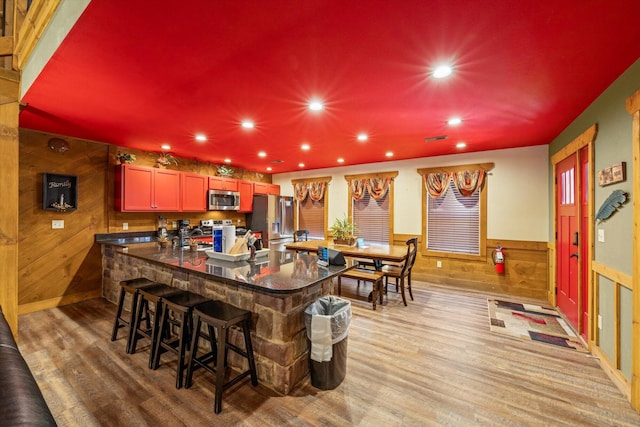 kitchen featuring wooden walls, a kitchen breakfast bar, appliances with stainless steel finishes, and light hardwood / wood-style flooring