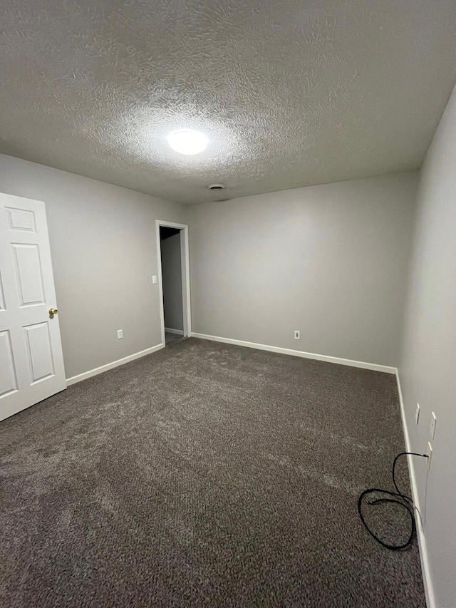 spare room featuring a textured ceiling and dark colored carpet