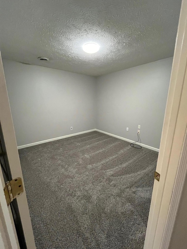 spare room with a textured ceiling and dark carpet