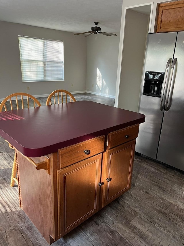 kitchen featuring stainless steel refrigerator with ice dispenser, dark hardwood / wood-style flooring, ceiling fan, and a kitchen island