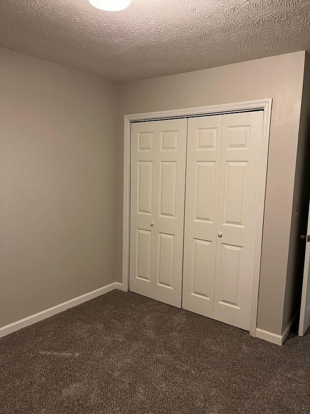 unfurnished bedroom featuring a textured ceiling, a closet, and dark colored carpet