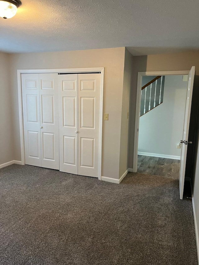 unfurnished bedroom with a textured ceiling, a closet, and dark carpet