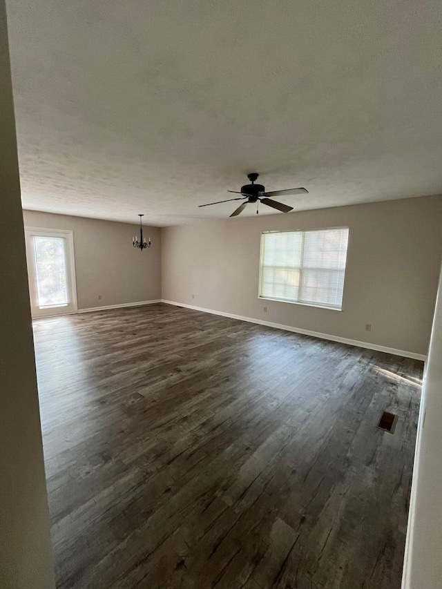 empty room with dark hardwood / wood-style flooring and ceiling fan with notable chandelier