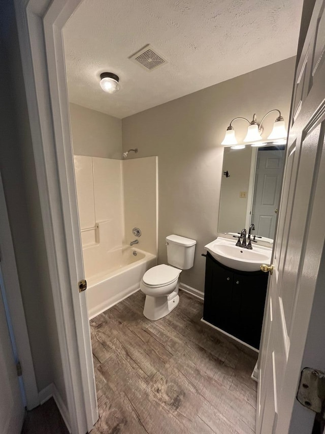 full bathroom featuring toilet, vanity, washtub / shower combination, wood-type flooring, and a textured ceiling