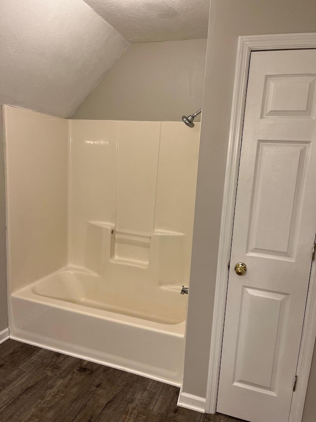 bathroom featuring vaulted ceiling,  shower combination, a textured ceiling, and hardwood / wood-style floors