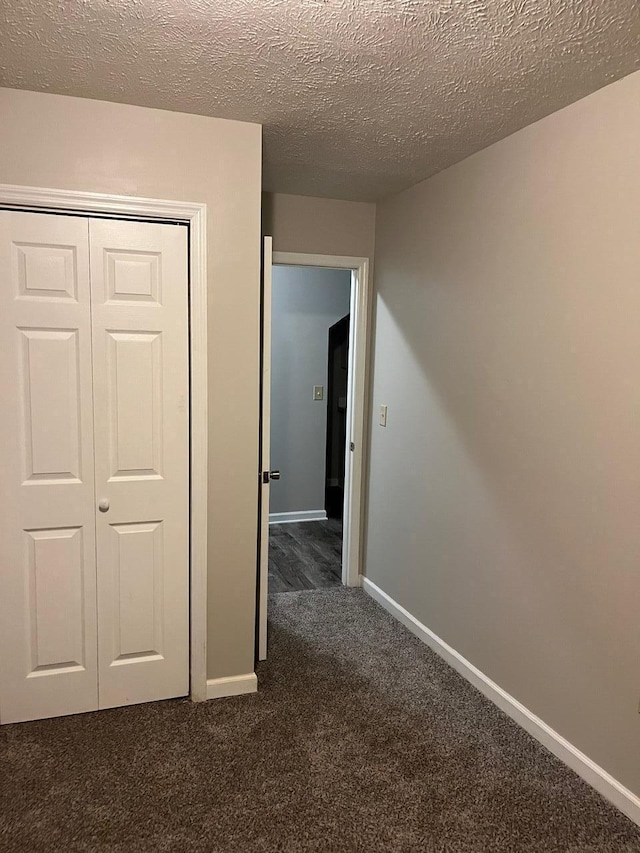 hallway with a textured ceiling and dark colored carpet