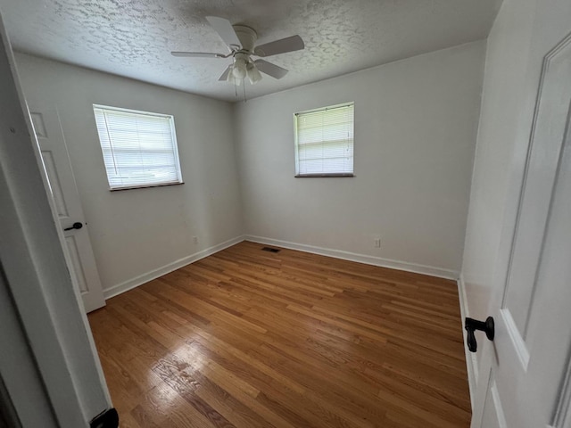 unfurnished bedroom featuring a textured ceiling, multiple windows, baseboards, and wood finished floors
