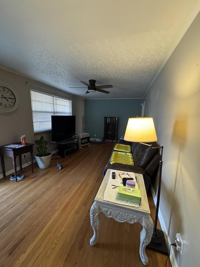 living room with ceiling fan, a textured ceiling, crown molding, wood finished floors, and baseboards