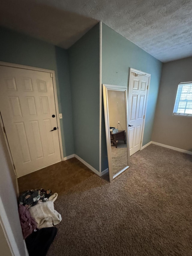 entrance foyer featuring baseboards, a textured ceiling, and dark carpet