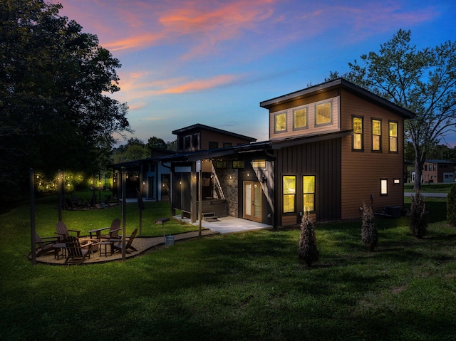 back of property at dusk with board and batten siding, a patio area, a yard, and a hot tub