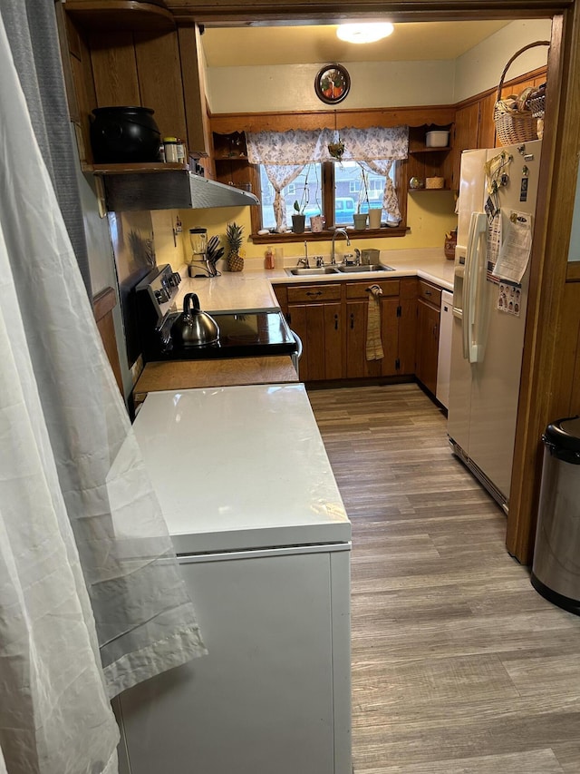 kitchen with white appliances, exhaust hood, sink, decorative light fixtures, and light hardwood / wood-style floors