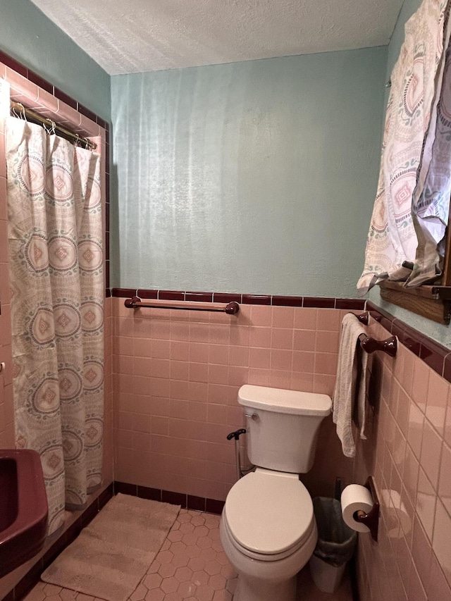 bathroom with tile patterned floors, a shower with curtain, a textured ceiling, tile walls, and toilet