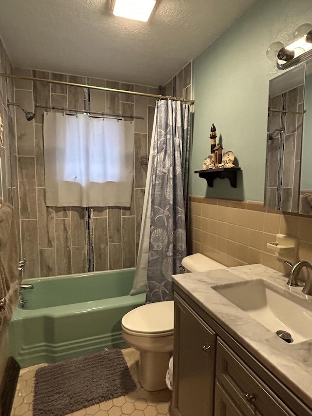 full bathroom featuring a textured ceiling, toilet, shower / bath combo with shower curtain, vanity, and tile walls