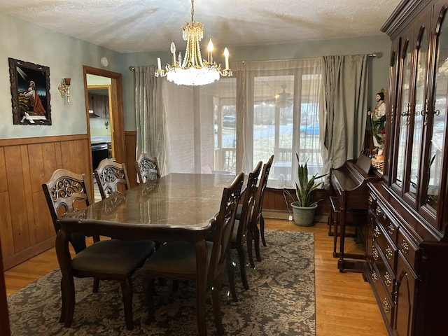 dining space featuring a textured ceiling, light hardwood / wood-style floors, a notable chandelier, and wood walls