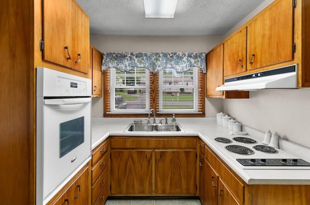 kitchen featuring under cabinet range hood, white appliances, a sink, brown cabinets, and light countertops