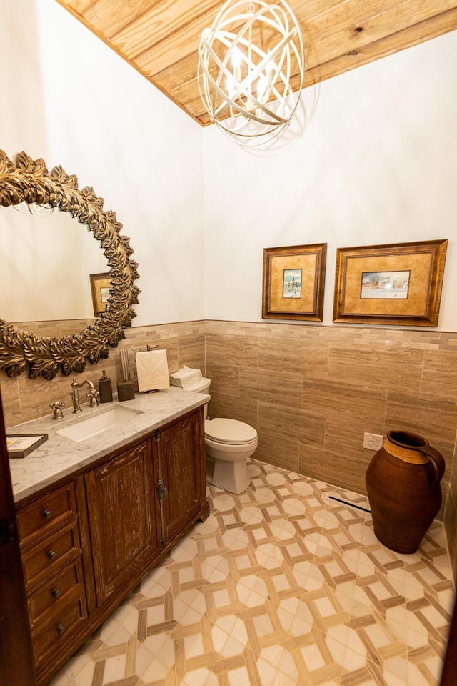 bathroom with tile patterned flooring, a chandelier, toilet, vanity, and tile walls