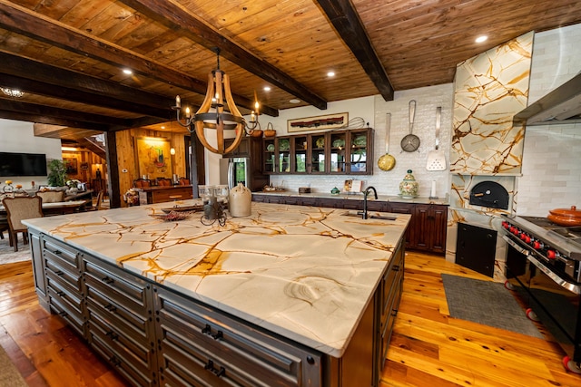 kitchen with beam ceiling, dark brown cabinetry, an island with sink, and wood ceiling