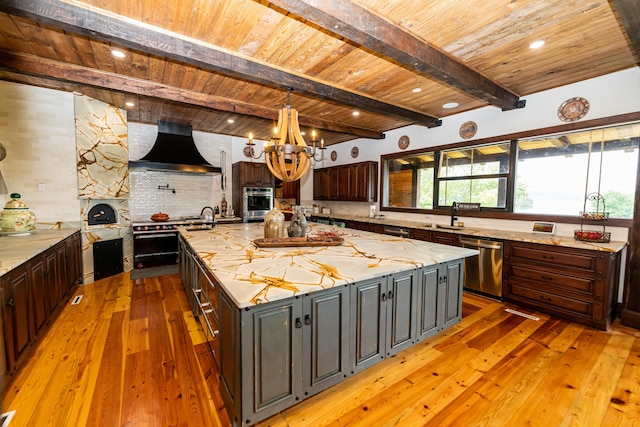 kitchen featuring a center island, wall chimney exhaust hood, stainless steel appliances, light stone counters, and decorative backsplash