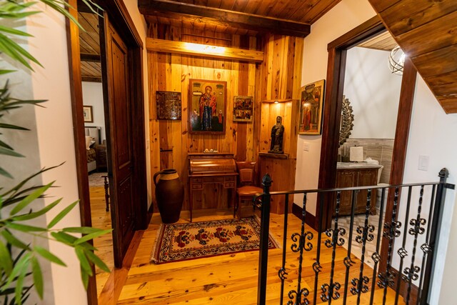 hallway with beamed ceiling, wooden walls, light hardwood / wood-style floors, and wooden ceiling