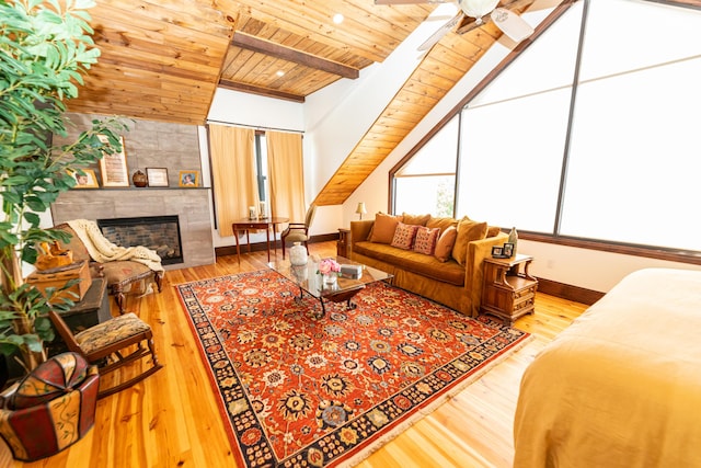 living room with ceiling fan, vaulted ceiling with beams, light hardwood / wood-style flooring, a tiled fireplace, and wood ceiling