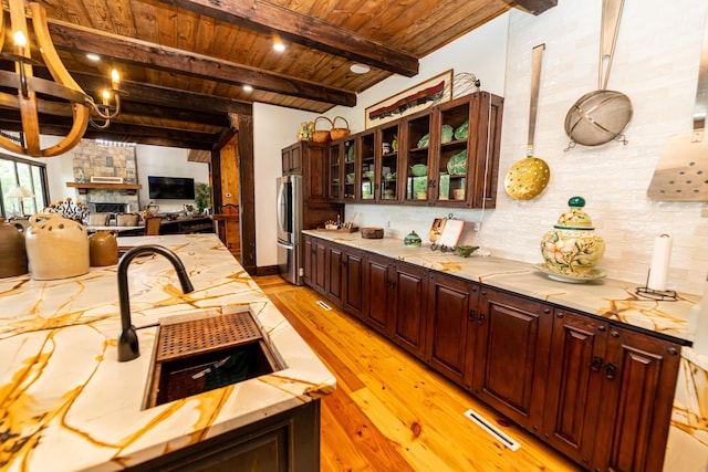 kitchen with wooden ceiling, a fireplace, beamed ceiling, light hardwood / wood-style floors, and stainless steel refrigerator