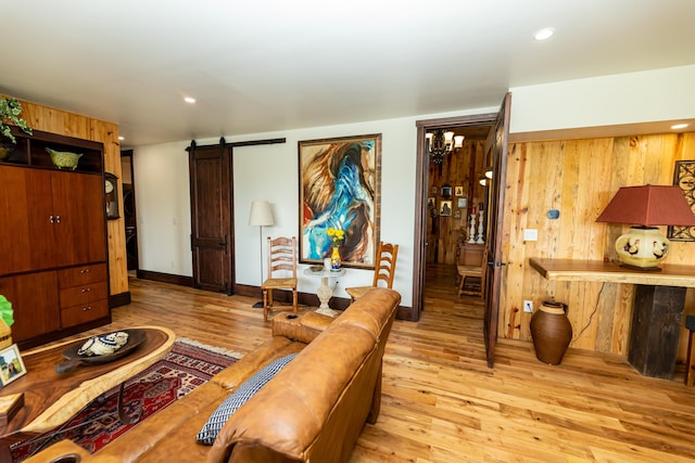 living room with a chandelier, a barn door, light hardwood / wood-style floors, and wood walls