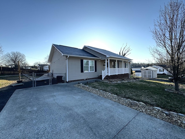 single story home featuring an outbuilding, fence, a porch, a front lawn, and a storage shed