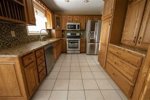 kitchen featuring light stone countertops, backsplash, stainless steel appliances, sink, and light tile patterned floors