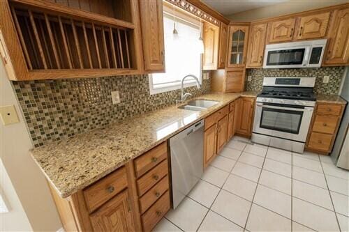 kitchen with sink, light tile patterned floors, tasteful backsplash, light stone counters, and stainless steel appliances