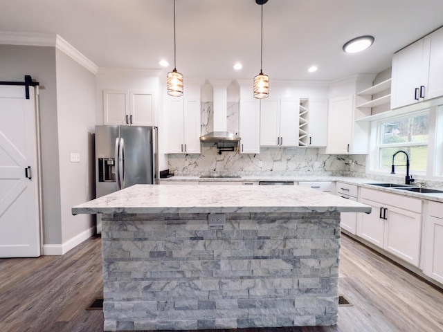 kitchen featuring open shelves, a barn door, a kitchen island, a sink, and wall chimney exhaust hood