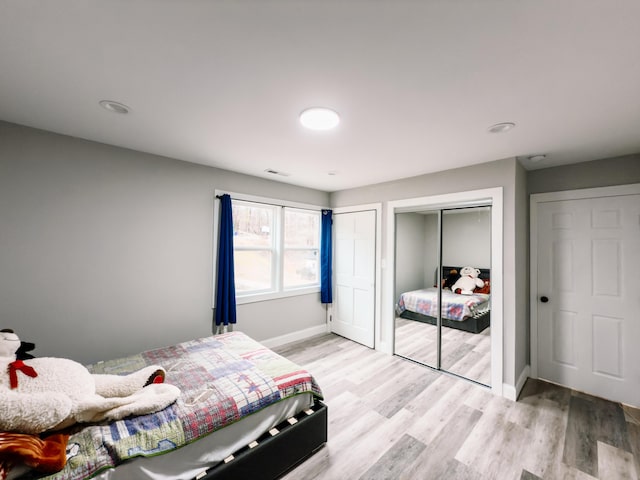 bedroom with light wood-type flooring, baseboards, visible vents, and two closets